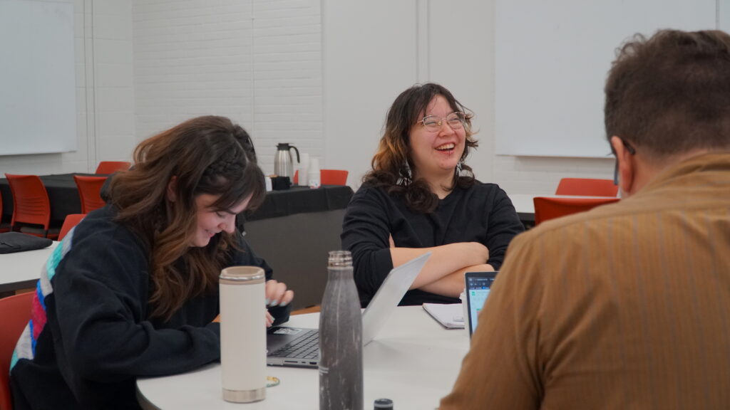 Three workshop participant's sitting at a table and laughing.