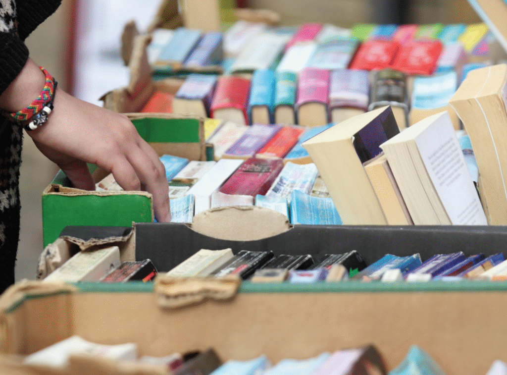 A hand riffling through colourful stacks of used books on a table.