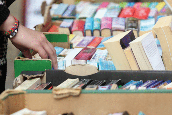 A hand riffling through colourful stacks of used books on a table.