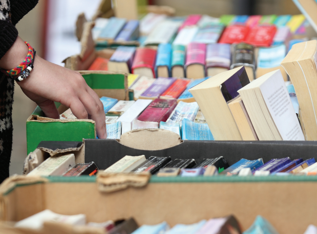 A hand riffling through colourful stacks of used books on a table.