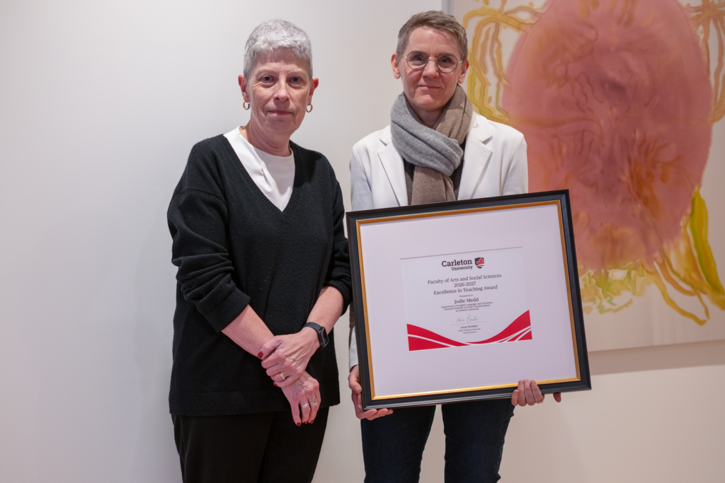 Jodie Medd holding a framed award certificate while standing beside Anne Bowker. 