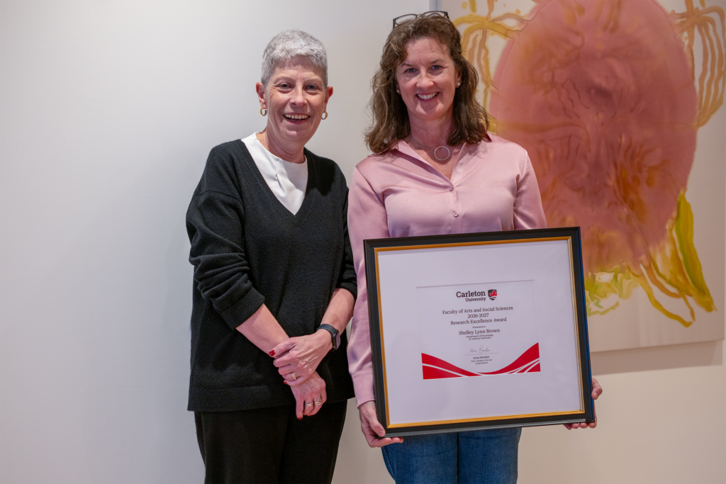 Shelley Brown holding a framed award certificate while standing beside Anne Bowker. 