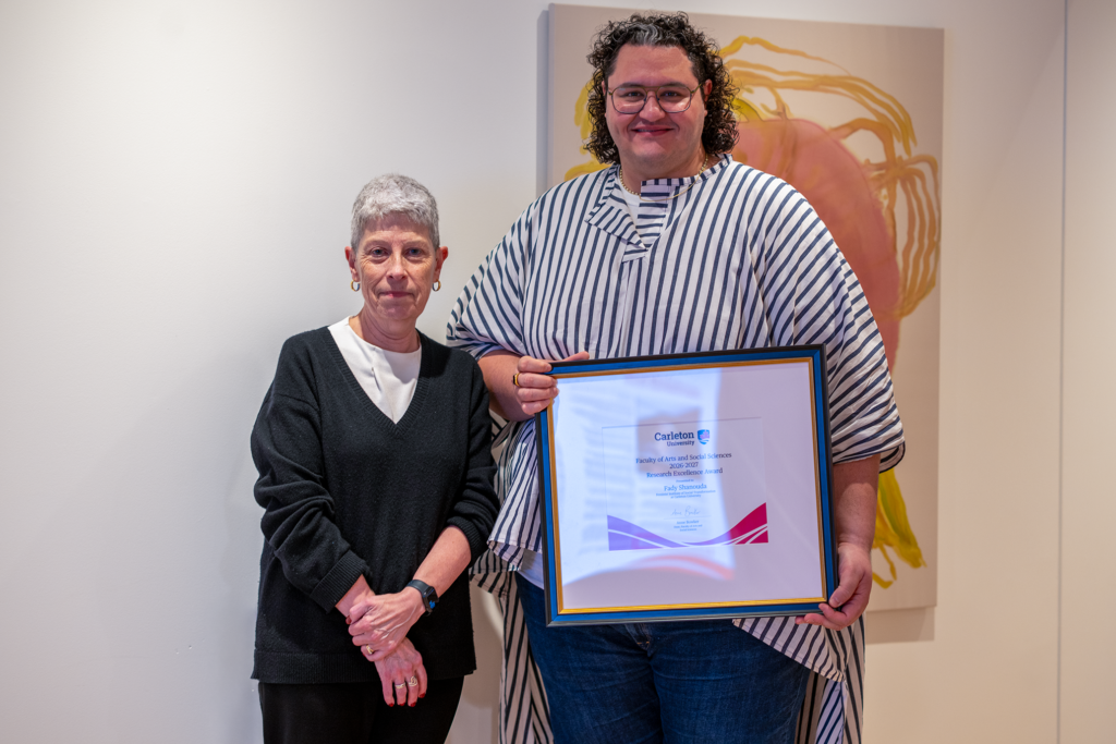 Fady Shanouda holding a framed award certificate while standing beside Anne Bowker. 