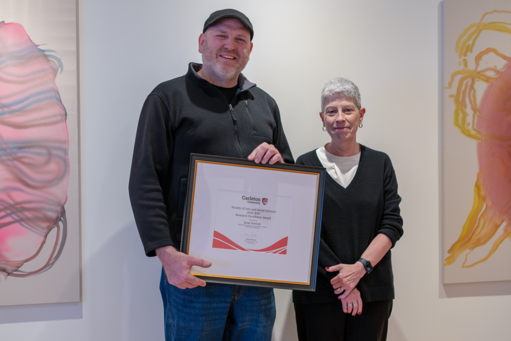 Jesse Stewart holding a framed award certificate while standing beside Anne Bowker. 