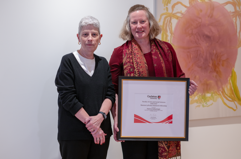 Patricia Ballamingie holding a framed award certificate while standing beside Anne Bowker. 