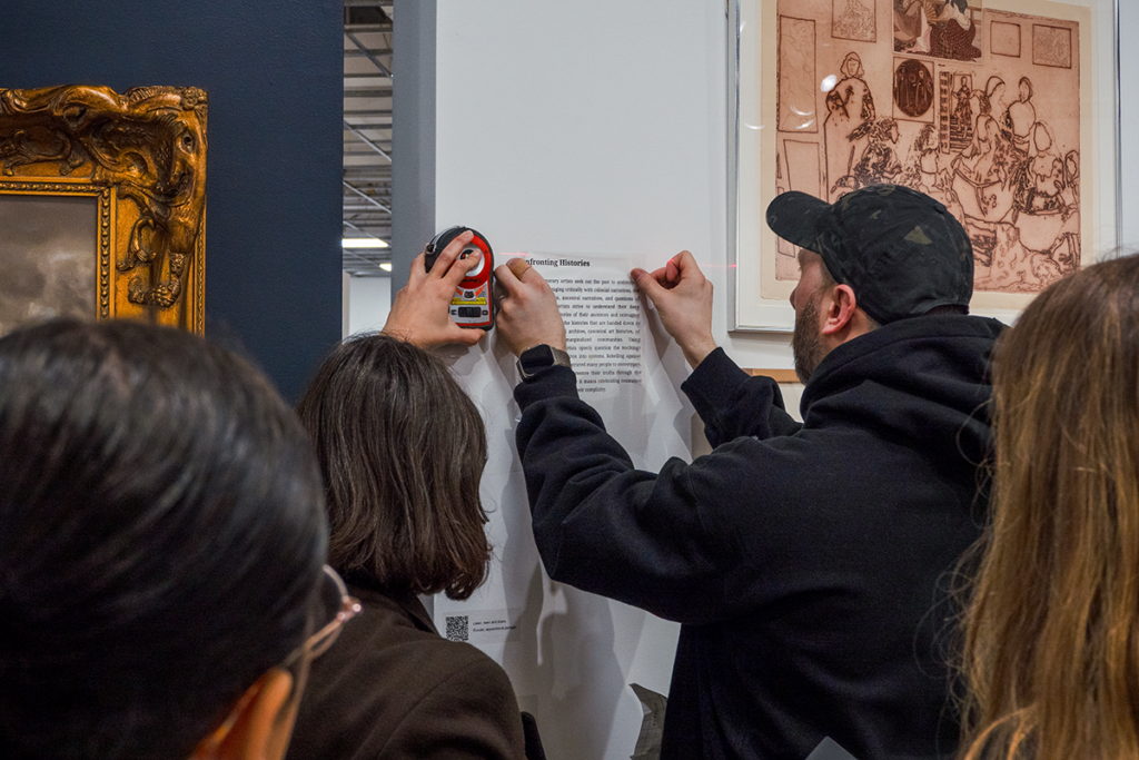 Two people installing a label next to a painting, while two others look on.