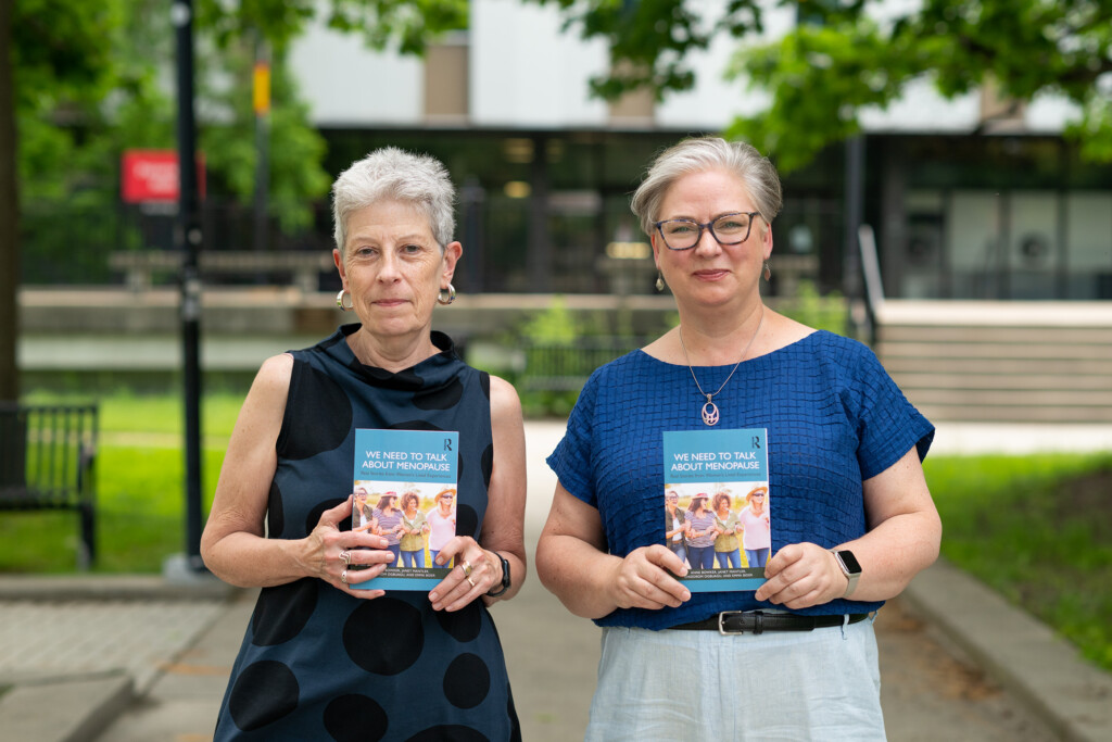 Anne Bowker and Janet Mantley standing side by side in the university's quad, each holding a copy of a book.