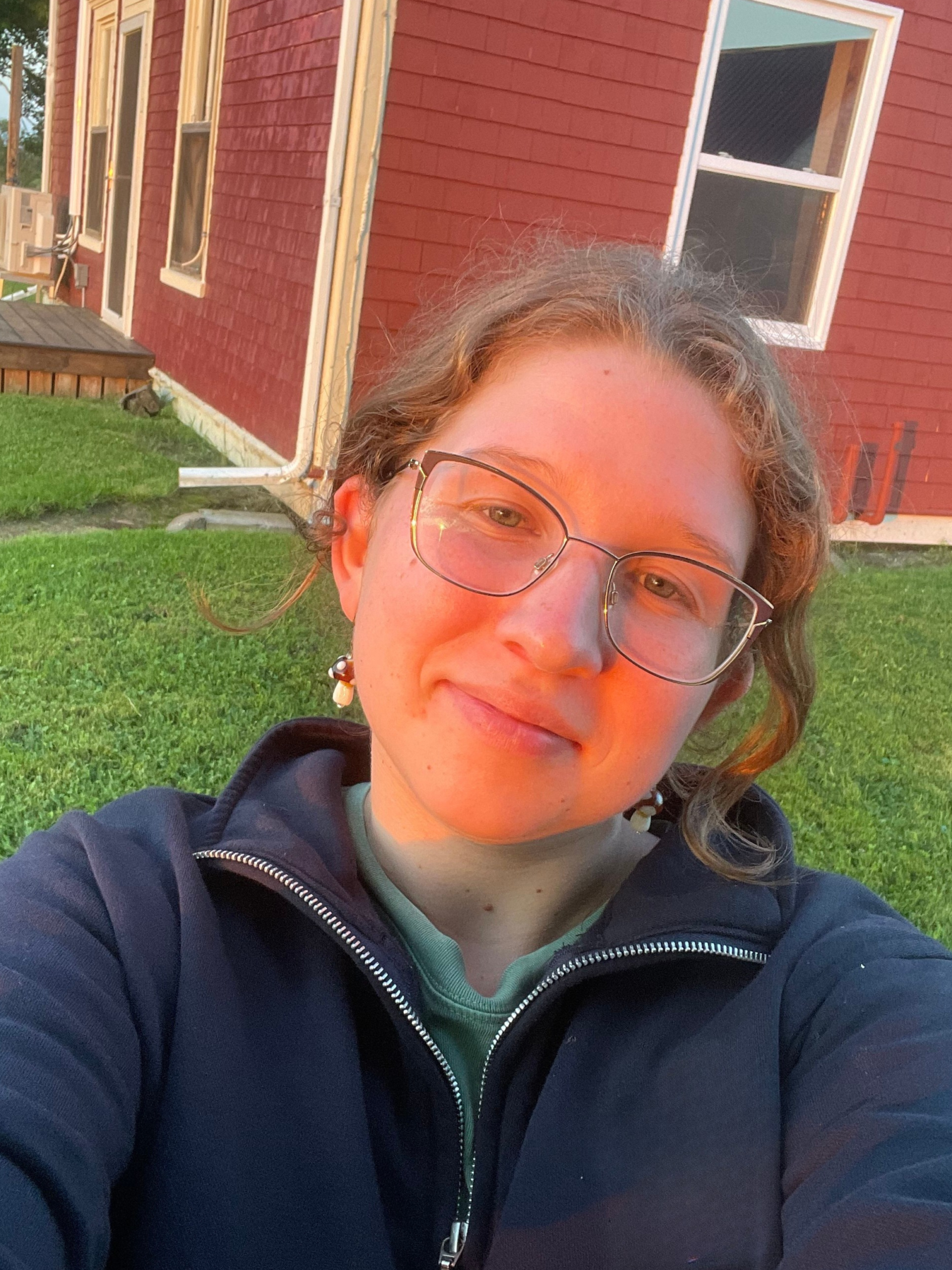 Student Ambassador in navy sweater with glasses, i front of red cottage