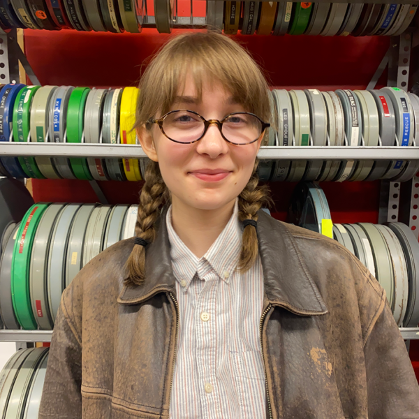 Student Ambassador with glasses and leather jacket, standing in front of film reels