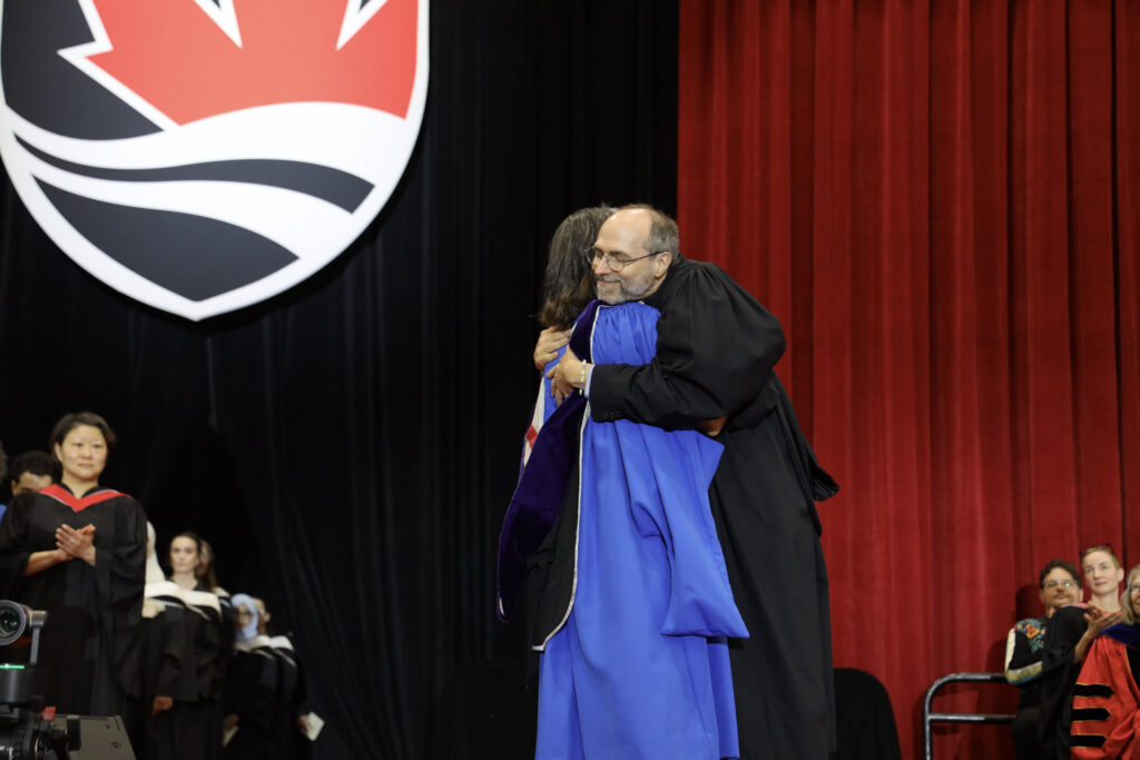 A faculty member and a doctoral student hug on stage at Convocation.