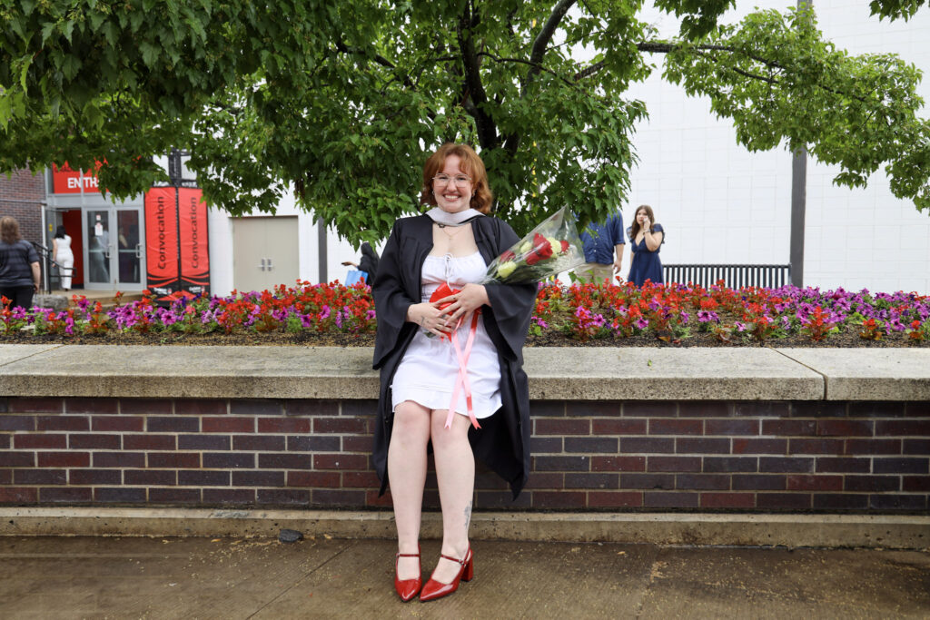 A graduate holding flowers.