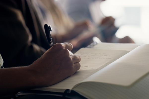 Someone taking notes by hand while sitting in a meeting.