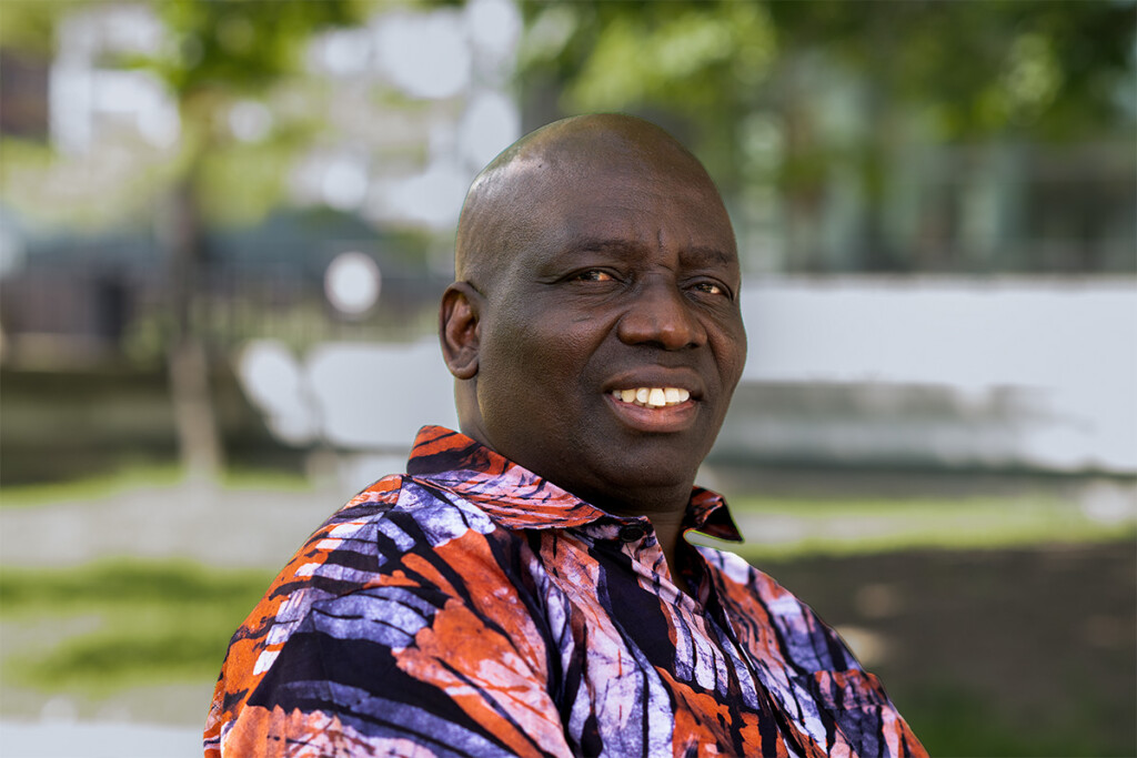 Samuel Ojo Oloruntoba sitting on a bench in the Carleton quad.