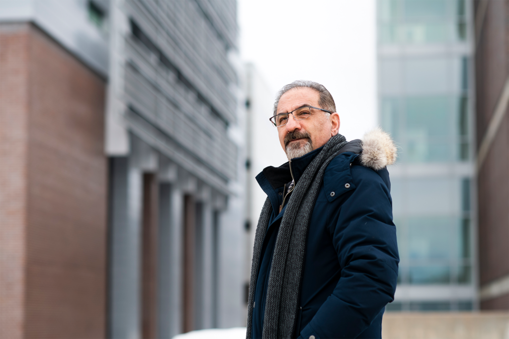 Jaffer Sheysholislami wearing glasses, a dark winter coat with a fur-trimmed hood, and a gray scarf.