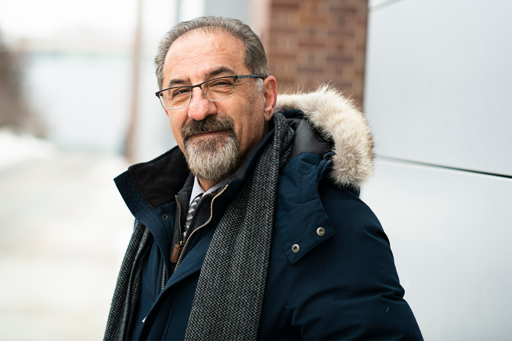 Jaffer Sheysholislami wearing glasses, a dark winter coat with a fur-trimmed hood, and a gray scarf.