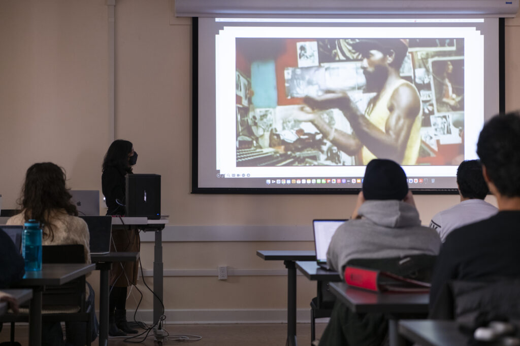 Students in the course Race and Representation in the Arts sit in a dark classroom watching a film. In the still, Lee Scratch Perry, a Dub musician, is in his recording studio.
