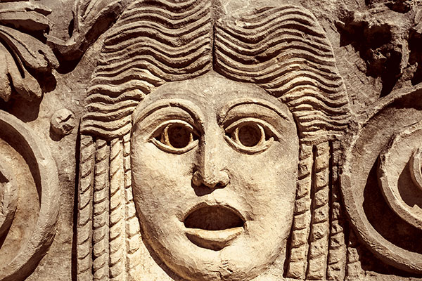 Roman theatrical mask or goddess in Greek mythology. Ancient mask in a Greek theatre, relief on stone wall. Decoration of theater for tragedy performance, classic art and Antique culture of Europe.