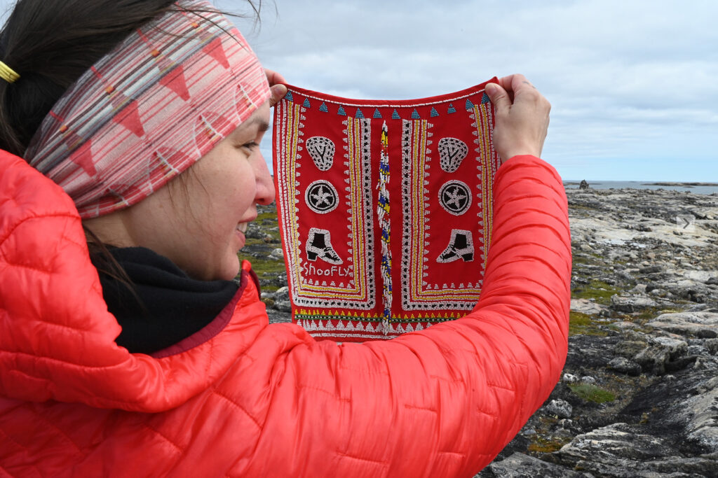 Krista Ulujuk Zawadski holds up beadwork that was replicated from the original by Nivisannaaq, which was beaded at Qatiktalik. Replica beadwork owned by Isuma. Photo credit: Maggie Putulik.