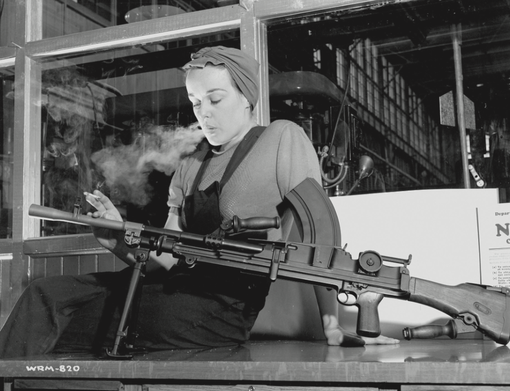 Unknown photographer. Veronica Foster, an employee of John Inglis Co. Ltd. and known as “The Bren Gun Girl” posing with a finished Bren gun in the John Inglis Co. Ltd. Bren gun plant, Toronto. 10 May 1941. Contemporary print from vintage negative. National Film Board of Canada. Photothèque / Library and Archives Canada e000760453.