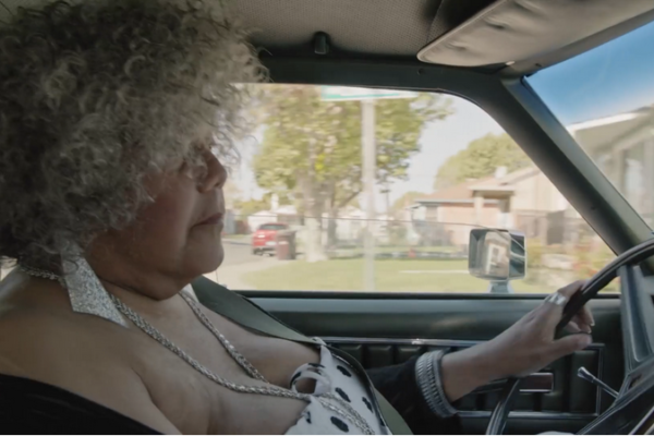 Still from Major! Miss Major, a Black trans woman in a curly grey wig, driving a car.
