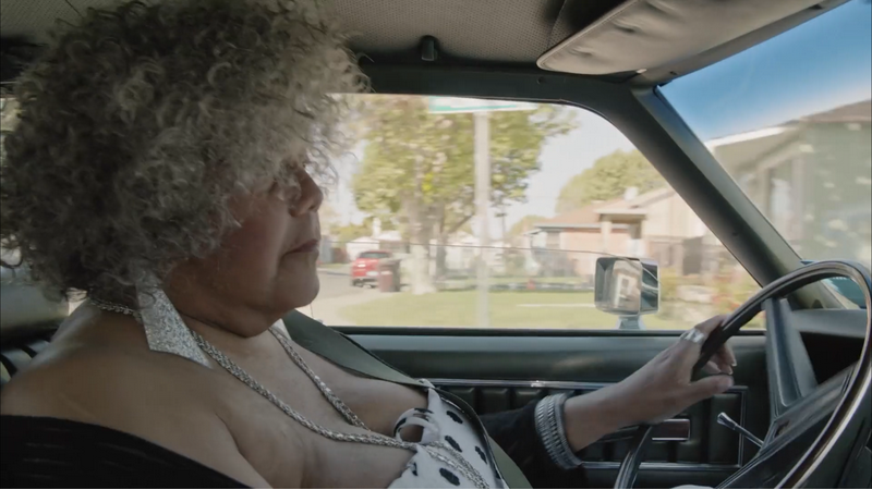 Still from Major! Miss Major, a Black trans woman in a curly grey wig, driving a car.
