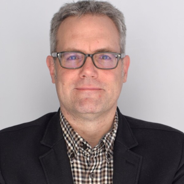 Man in black blazer with checkered dress shirt smiling