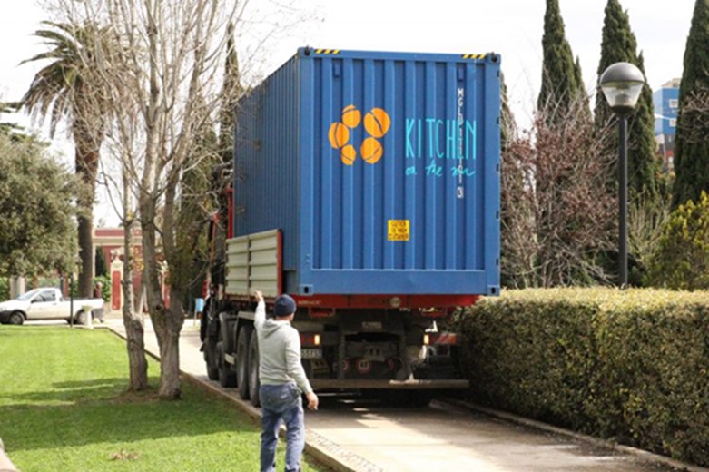 A blue shipping container is loaded on the back of a truck and driven away. 