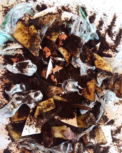 A mixture of coffee grounds, plastic bags, and compost on a sheet of white paper.