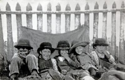 Indigenous children sit aligned agains a fence.