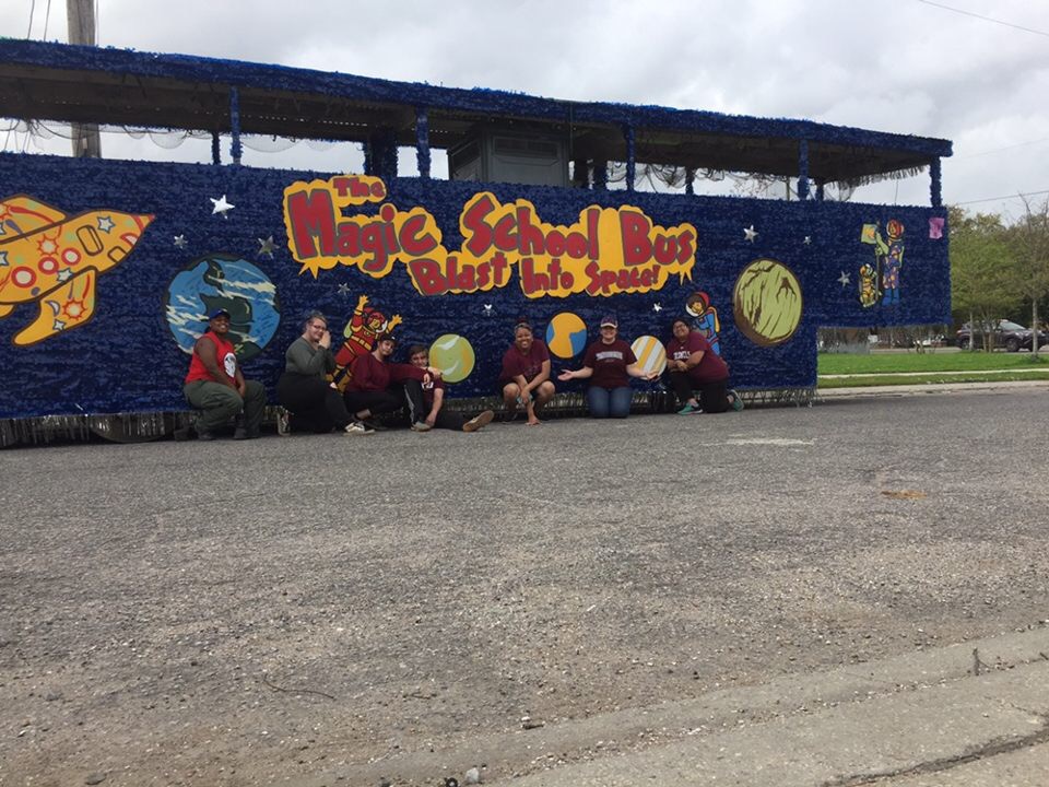 Students and teacher pose in front of a float of the Magic School Bus.