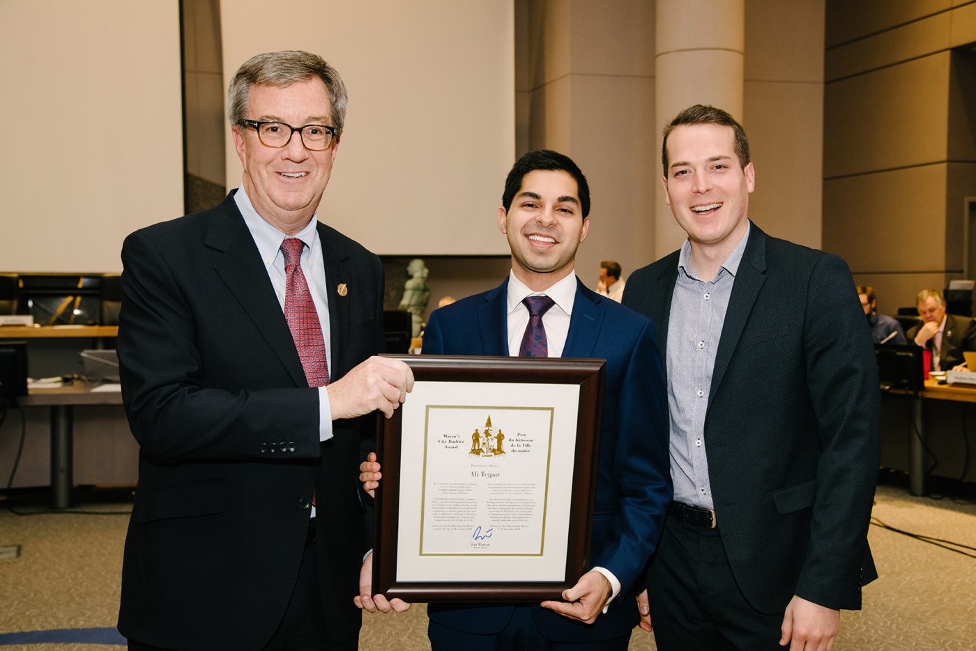 Ali Tejpar holds a certificate with Jim Watson and Mathieu Fleury on either side of him.