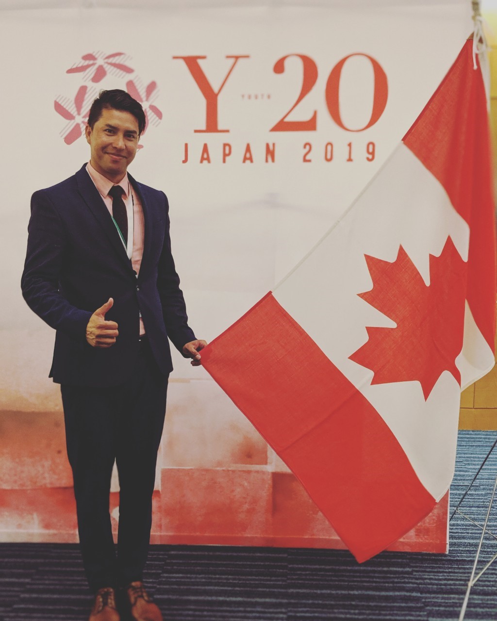 Ali Bahman stands next to a Canadian flag and in front of a sign for the G20 summit in Japan.
