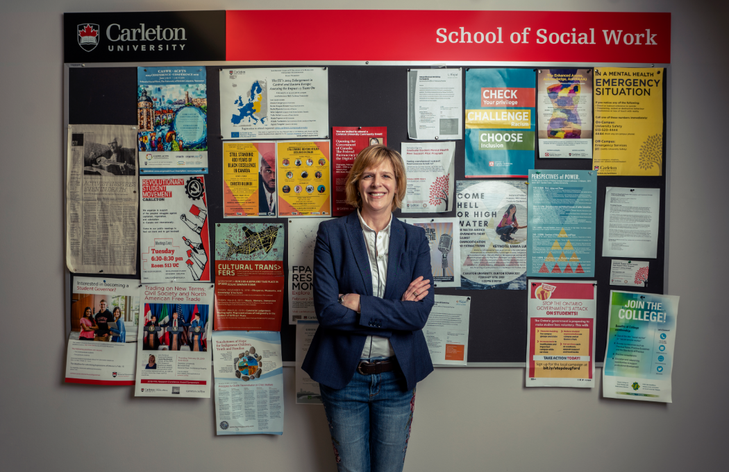 Professor Sarah Todd stands in front a bulletin board in the School of Social Work.