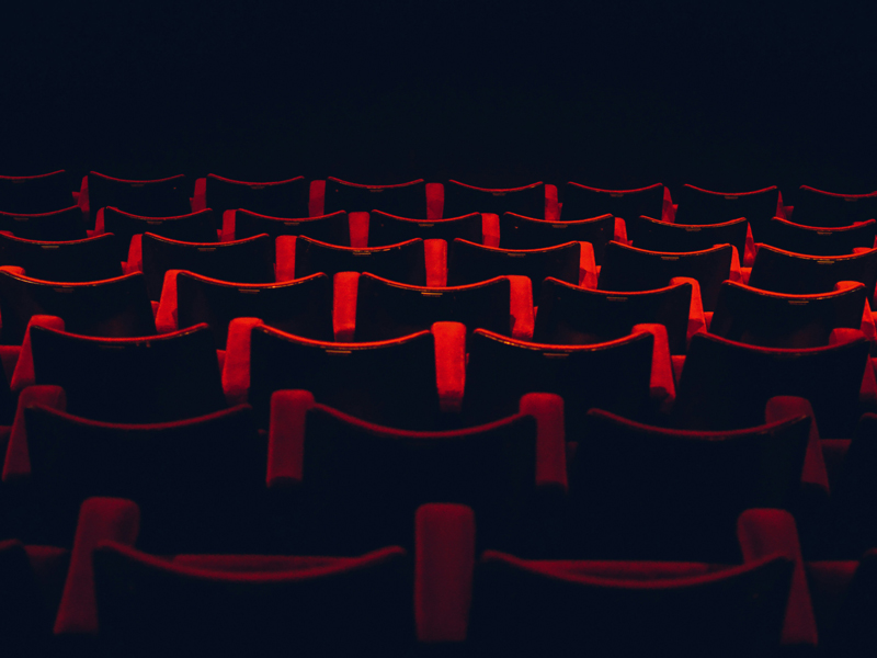 Rows of red movie theatre seats in the dark.