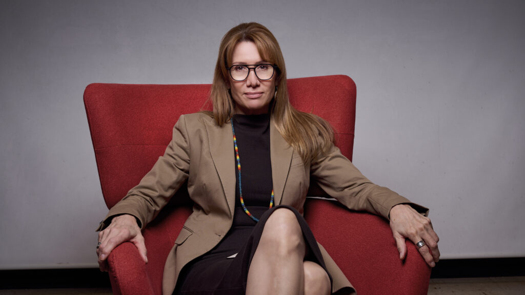 Jane Dickson sits in a red chair against a light grey backdrop
