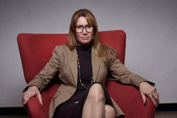 Jane Dickson sits in a red chair against a light grey backdrop