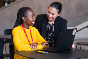 A student working on a laptop looks at a professor over their shoulder