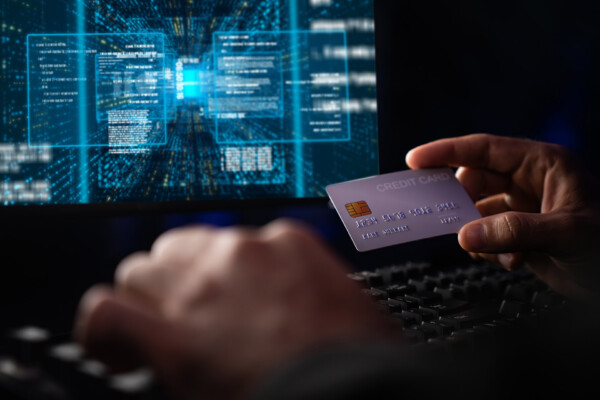 Photo of a computer screen and a hand holding a credit card