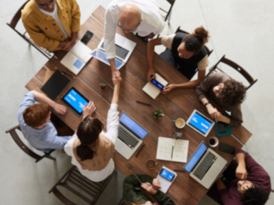 Eight people working around a desk with laptops and two students shaking heads collaborating