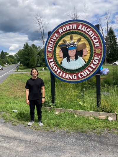 Richard standing outside, next to a sign for the College at Akwesasne