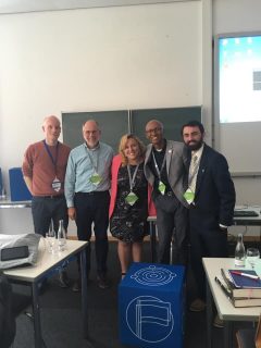 five people standing in front of blackboard in classroom