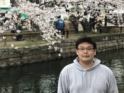 Ken Yoshida in front of cherry blossom trees