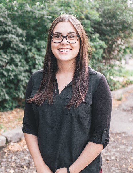 Tyla Betke standing outside in front of green hedge