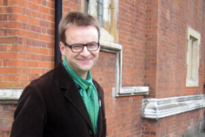 Dr. Tim Cresswell standing outside in front of a brick wall