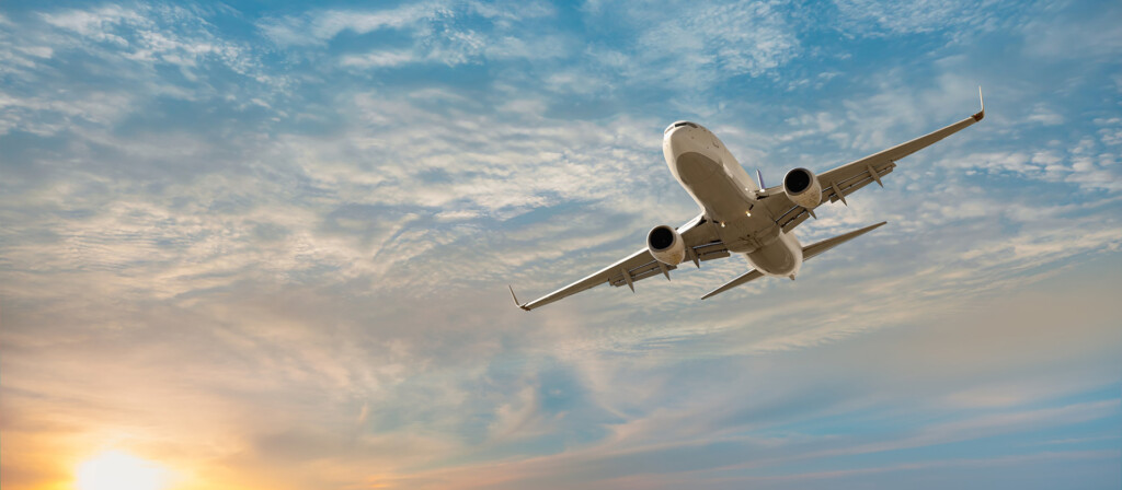 A commercial airplane flying with the sun visible in the distance.
