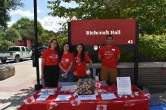 Four students sitting in front of a Richcraft Hall sign, standing behind a table covered in Canadian flags and prizes.