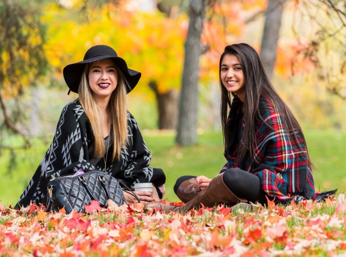 Two students sit outside surrounded by fall leaves.