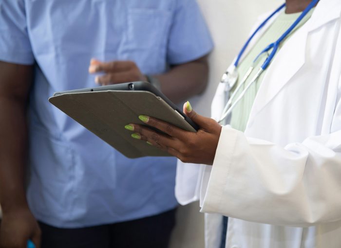 A doctor wearing a white coat and stethoscope holds a tablet.