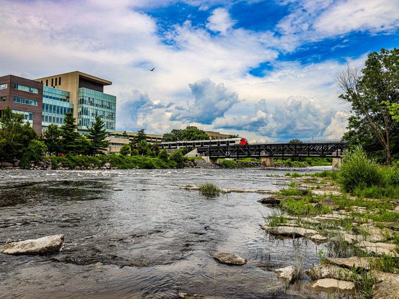 Carleton's campus with a view of the Rideau River, Richcraft Hall and the O-Train during summer.