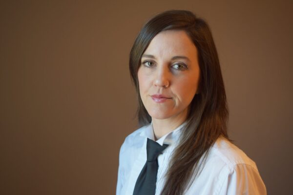 Prof. Stacy Douglas in a tie and white dress shirt, against a medium brown background